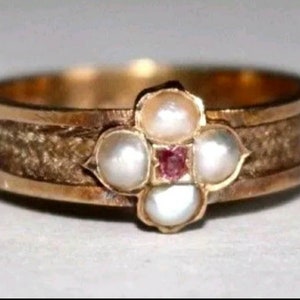 Puede incluir: Un anillo de oro con un grupo de cinco perlas y una pequeña piedra preciosa roja en el centro. El anillo tiene una banda texturizada.