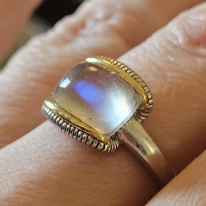 May include: A silver ring with a gold band and a large, clear moonstone.