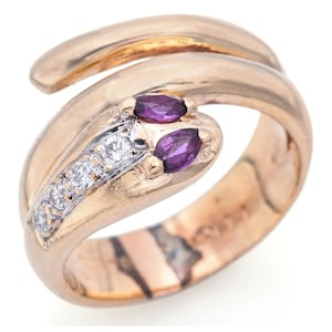 May include: A gold snake ring with two purple gemstones and a row of clear diamonds. The ring is made of 14k gold and is a size 7.