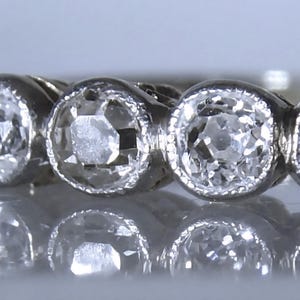 May include: A silver-toned metal ring featuring five round, faceted clear stones set in a row. Each stone is secured within a circular bezel setting with a fine milgrain edge detail along the perimeter of the metal surrounding the stones.
