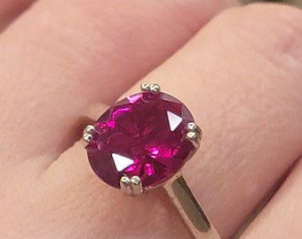 May include: A silver ring with a large, oval-shaped, deep pink gemstone.