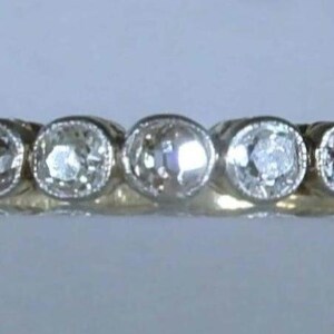 May include: A gold ring featuring five round, clear, faceted stones set in a row. Each stone is secured in a circular bezel setting with a milgrain edge. The band is smooth and polished, showcasing a consistent yellow gold tone throughout the design.