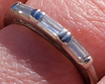 Könnte beinhalten: Ein Ring aus silberfarbenem Metall mit einer Reihe von drei klaren, rechteckigen Baguette-Steinen, die horizontal entlang des Rings angeordnet sind. Die Steine werden von kleinen Metallfassungen an ihrem Platz gehalten.
