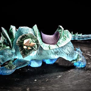 May include: A blue and green ice wolf figurine with a saddle. The wolf is sculpted in a running pose with its mouth open and fangs showing. The saddle is purple and has a green and gold design.
