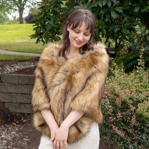 May include: A faux fur shawl in a brown and tan color with a soft, fluffy texture. The shawl is draped over the shoulders of a person wearing a white dress.