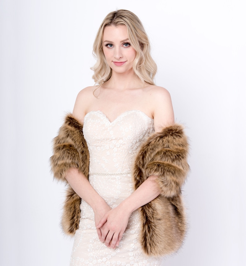 May include: A brown faux fur shawl with a long, flowing design. The shawl is worn over a white strapless dress with delicate lace detailing.