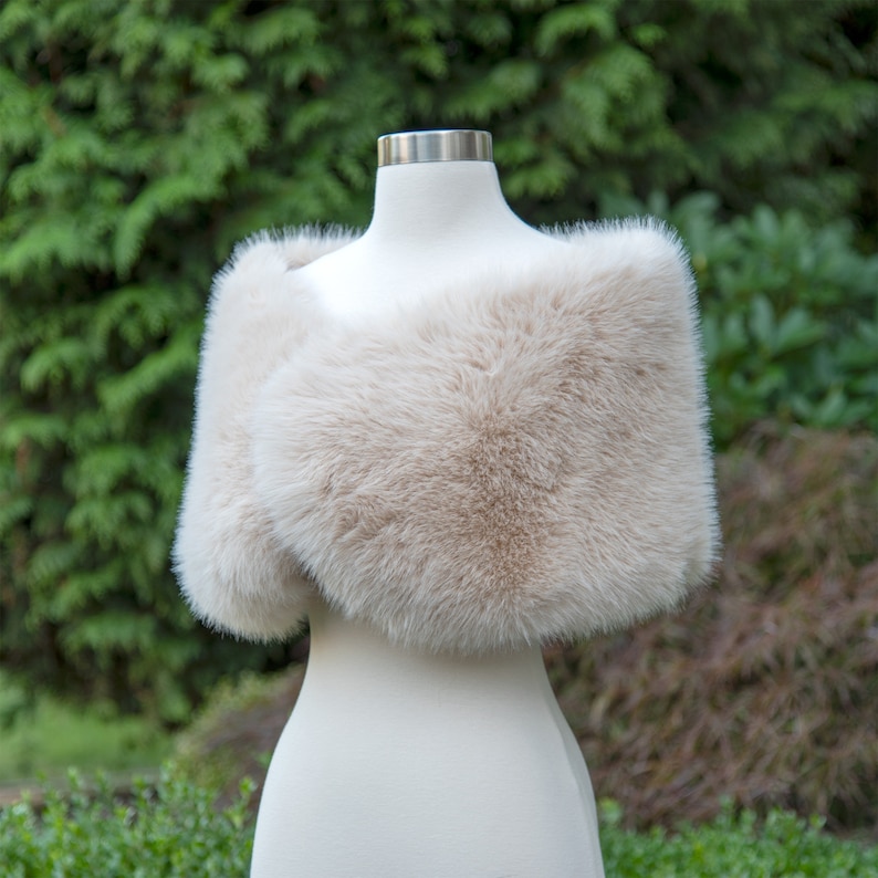 May include: A cream-coloured faux fur shawl draped over a white mannequin. The shawl is soft and fluffy, and it would be perfect for a wedding or other special occasion.
