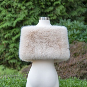 May include: A cream-coloured faux fur shawl, displayed on a white mannequin against a green background.