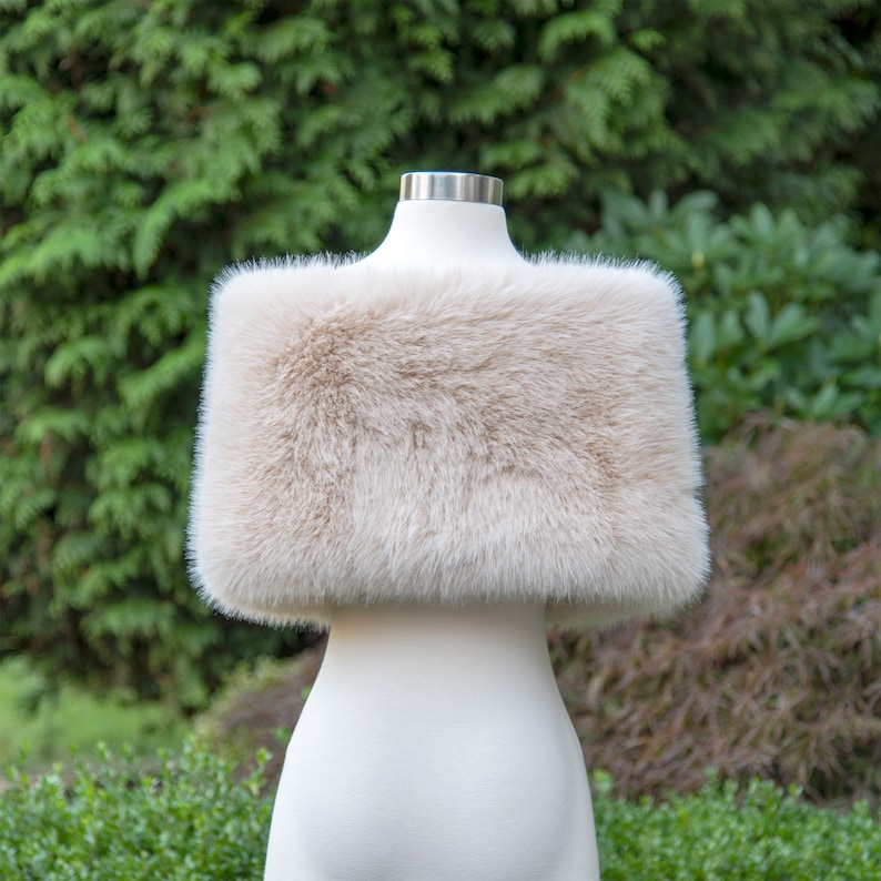 May include: A cream-coloured faux fur shawl, displayed on a white mannequin against a green background.