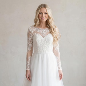 May include: A white wedding dress with a sweetheart neckline and long, sheer lace sleeves. The bodice features intricate floral embroidery, and the skirt is made of flowing tulle. The dress is designed for a formal occasion.
