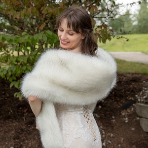 May include: A white faux fur shawl draped over a person's shoulders. The shawl is soft and fluffy, and it would be perfect for a wedding or other special occasion.