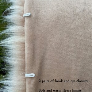 May include: Close-up of the inside of a beige faux fur jacket. The jacket has a soft fleece lining and two pairs of hook and eye closures.