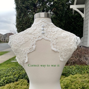 May include: White lace bridal bolero with pearl embellishments and three pearl buttons on the back. "Correct way to wear it" is written below the bolero.