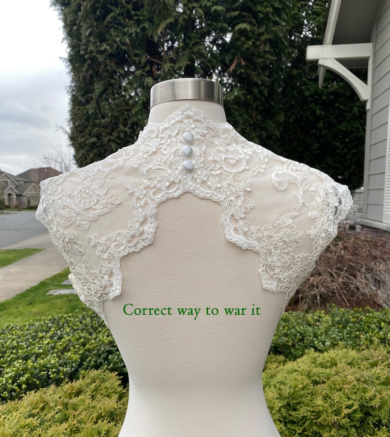 May include: White lace bridal bolero with pearl embellishments and three pearl buttons on the back. "Correct way to wear it" is written below the bolero.