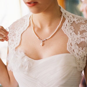 May include: A bride wearing a white lace wedding dress with a pearl necklace and a single pearl pendant.