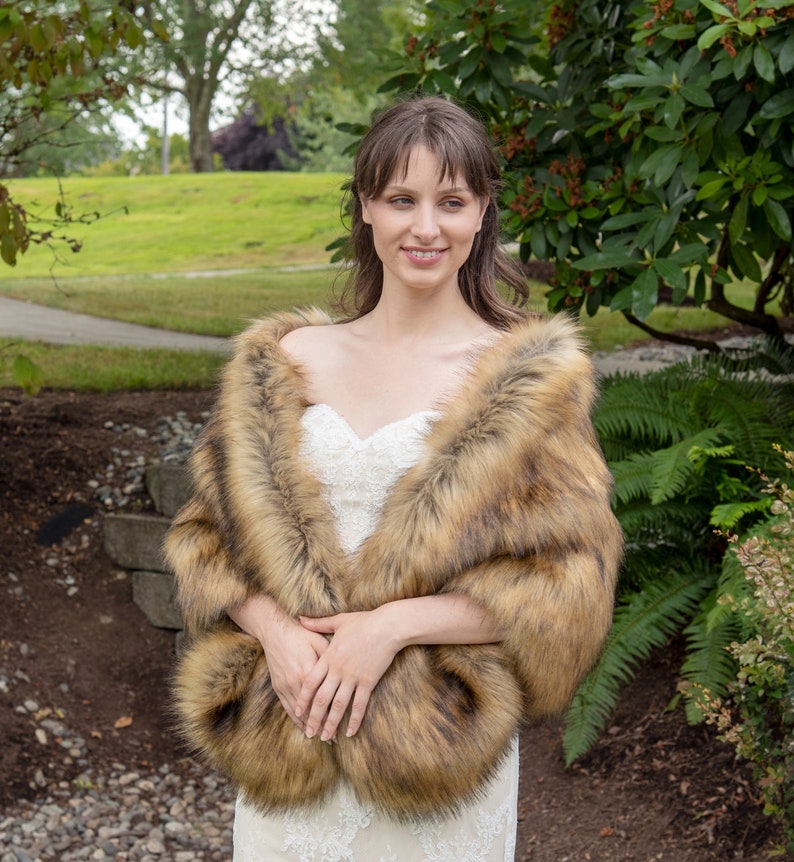 May include: A woman wearing a brown faux fur shawl over a white lace wedding dress. The shawl has a long, flowing design and is made of soft, plush faux fur.