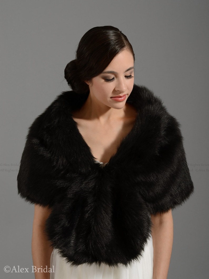 May include: A black faux fur shawl with a soft, fluffy texture. The shawl is draped around the shoulders of a person wearing a white dress.