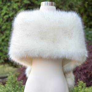 May include: A white faux fur shawl with a fluffy texture. The shawl is draped over a white mannequin.