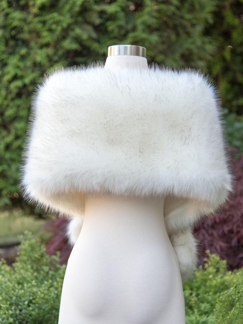 May include: A white faux fur shawl with a fluffy texture. The shawl is draped over a white mannequin.