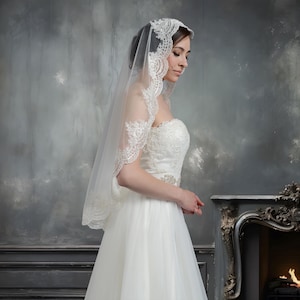 Pode incluir: Um v&eacute;u de noiva branco com uma delicada renda. O v&eacute;u &eacute; usado por uma pessoa com um vestido de noiva branco.