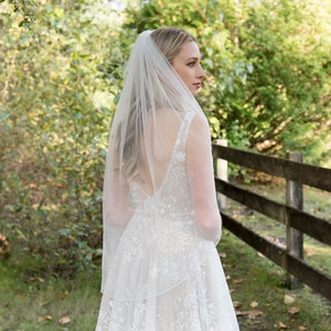 May include: A white bridal veil with a single layer of tulle, worn by a person with long blonde hair. The veil is simple and elegant, with a scalloped edge.