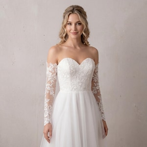 May include: A white floor-length gown featuring a sweetheart neckline and off-the-shoulder long sleeves. The bodice and sleeves are adorned with intricate white floral lace embroidery, while the skirt is made of a layered, sheer tulle fabric.