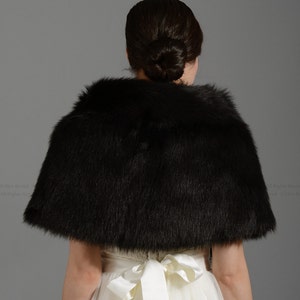 May include: A black faux fur bridal shawl with a satin ribbon tie. The shawl is worn over a white wedding dress.