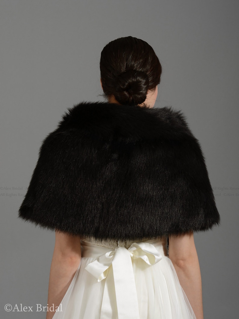 May include: A black faux fur bridal shawl with a satin ribbon tie. The shawl is worn over a white wedding dress.