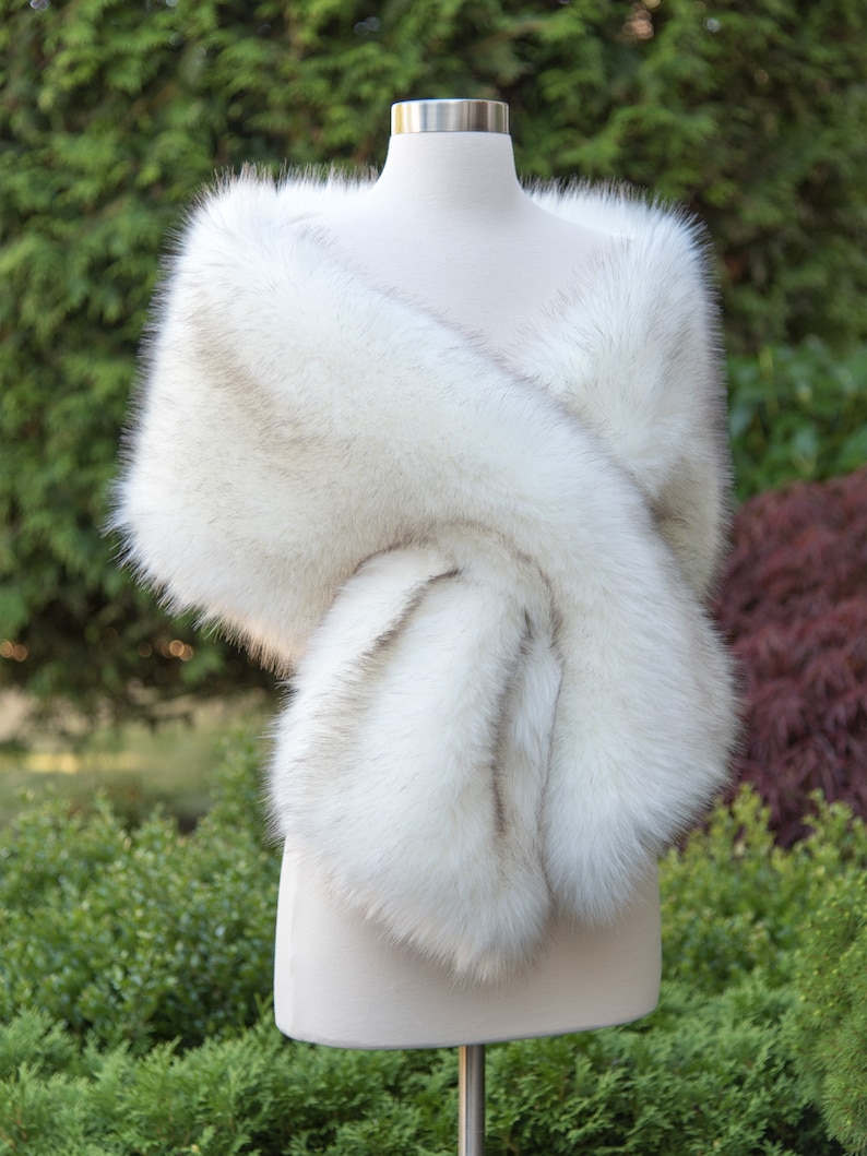 May include: A white faux fur shawl with a soft, fluffy texture. The shawl is draped over a mannequin and is perfect for adding a touch of elegance to any outfit.
