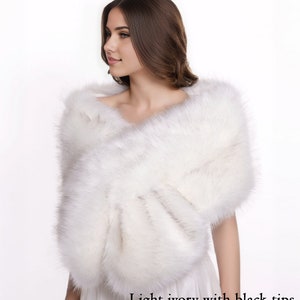 May include: A white faux fur shawl with black tips. The shawl is draped over a person's shoulders.