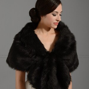 May include: A black faux fur shawl with a soft, fluffy texture. The shawl is draped over the shoulders of a person wearing a white dress.