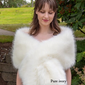 May include: A white faux fur shawl with a soft, fluffy texture. The shawl is draped over the shoulders of a person and is tied at the neck. The text "Pure ivory" is visible in the lower right corner of the image.