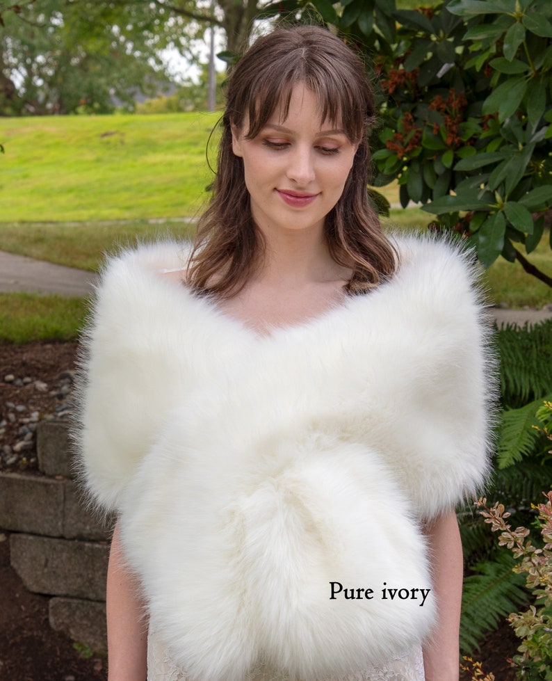 May include: A white faux fur shawl with a soft, fluffy texture. The shawl is draped over the shoulders of a person and is tied at the neck. The text "Pure ivory" is visible in the lower right corner of the image.