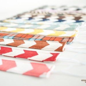 May include: A collection of fabric straps with various patterns, including plaid, chevron, and stripes. The straps are white with different colored designs and have white elastic loops attached to each end.