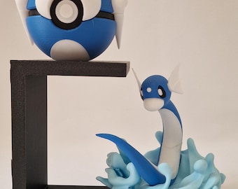 May include: A blue and white Poke Ball and a blue and white Dratini sculpture. The Dratini is emerging from a light blue water effect. The Poke Ball is perched on a black shelf. The Dratini is approximately 10 cm tall.