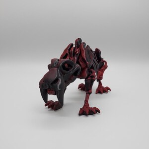 Peut inclure: Modèle imprimé en 3D d'un squelette de tigre à dents de sabre. Le modèle est principalement noir avec des accents rouges, mettant en valeur la structure squelettique. Le tigre est représenté en position de marche, avec ses crocs proéminents.