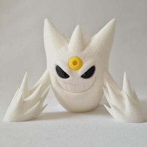 May include: A white, stylized figurine of a creature with a smiling face, black eyes, and a yellow circular detail. The figurine has sharp, pointed appendages and a textured surface, resembling a cartoon character.