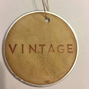 May include: A round, brown paper tag with a silver metal rim and a hole at the top. The tag has the word "VINTAGE" printed in red.