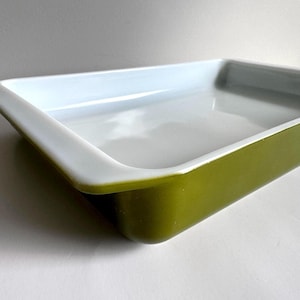 May include: A rectangular baking dish with a white interior and a green exterior. The dish has a smooth, glossy finish and a slightly curved rim. The dish is empty and appears to be unused.