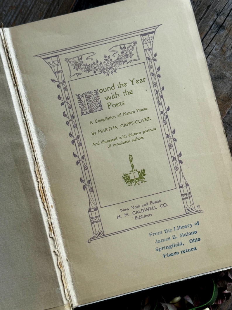 Pode incluir: Livro aberto intitulado "Round the Year with the Poets" de Martha Capps-Oliver. A capa apresenta desenhos florais e geom&eacute;tricos decorativos em um tom roxo suave. O livro &eacute; da biblioteca de James B. Malone, Springfield, Ohio.