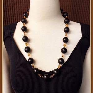 May include: A black and gold beaded necklace with large black beads and smaller gold beads. The necklace is on a black mannequin.