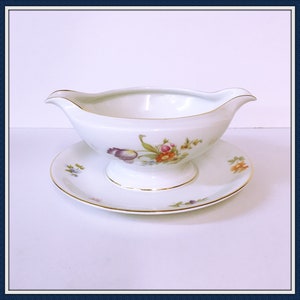 May include: White porcelain gravy boat with a floral design and a matching saucer. The gravy boat has a gold rim and the saucer has a gold rim and a gold band around the edge.