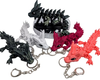 May include: Five different colored dragon keychains. The dragons are made of plastic and have a textured, scaly appearance. Each dragon is attached to a silver chain and a silver ring.