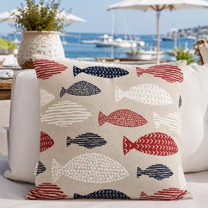 Peut inclure: Un coussin carré avec un fond beige présentant un motif répétitif de poissons stylisés en bleu marine, rouge et blanc. Les motifs de poissons incluent diverses textures telles que des points, des lignes horizontales et des chevrons.
