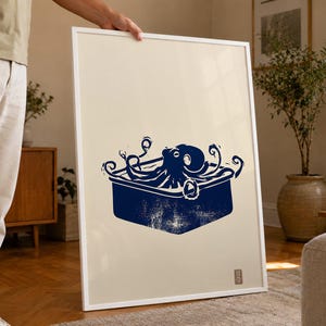 Könnte beinhalten: Ein gerahmter vertikaler Wandkunstdruck mit einer dunkelblauen Illustration im Tintenstil, die einen Oktopus in einem rechteckigen Behälter zeigt. Das Kunstwerk ist auf einem hellcremefarbenen Hintergrund und enthält ein kleines rotes Quadrat.