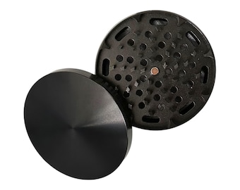 May include: A black metal grinder with a circular top and a bottom with a series of holes. The top is smooth and the bottom has a textured surface.