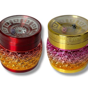 Pode incluir: Dois recipientes de moedor de metal com tema de cassino. O moedor vermelho tem uma base dourada e o moedor dourado tem uma base rosa. Ambos os moedores têm uma tampa transparente com uma roleta e dados no interior.
