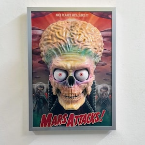 Peut inclure: Œuvre d'art encadrée représentant une tête d'extraterrestre sculptée en 3D du film "Mars Attacks!". L'extraterrestre a un grand cerveau, un visage en forme de crâne et des yeux rouges. L'affiche comprend le texte "Nice Planet. We'll Take It!" et "Mars Attacks!" en rouge.