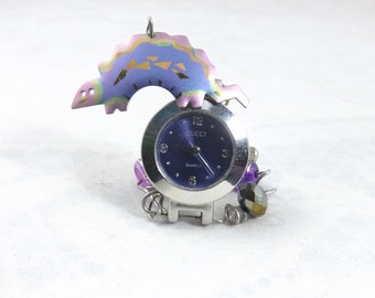 Miniature clock to fit any nook or a child's room with a colorful dinosaur charm and attractive silver and blue clockface and pretty beads.