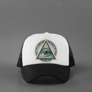 May include: A black and white trucker hat with a white front panel featuring a circular design with an eye inside a triangle. The hat has a black brim and mesh back.